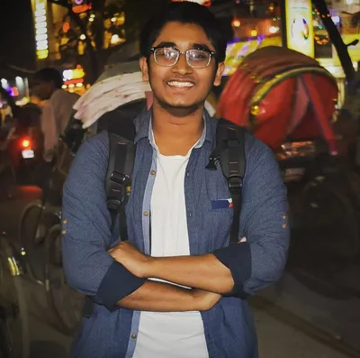 Saran Deb Nath smiling with arms crossed on a Dhaka street at night, rickshaws behind